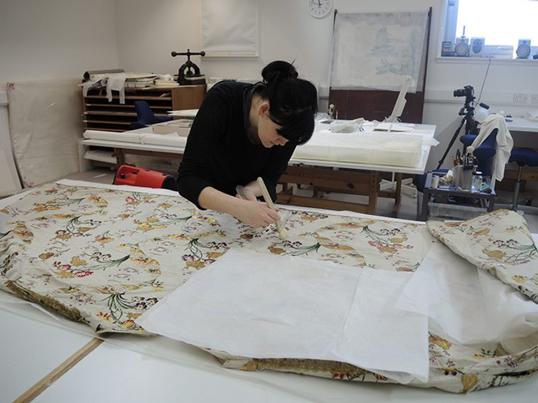 A conservator working on the cleaning and conservation of a gown with complex pattern designs.