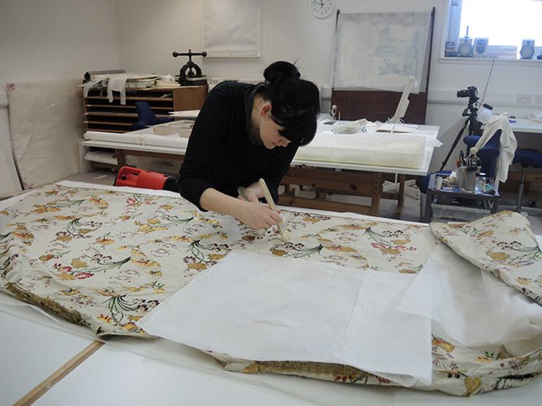 A conservator working on the cleaning and conservation of a gown with complex pattern designs.