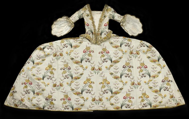 An extravagant gown with a wide skirt and complex pattern designs, laid flat against a dark background.
