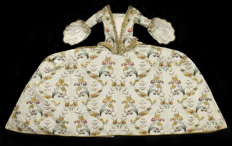 An extravagant gown with a wide skirt and complex pattern designs, laid flat against a dark background.