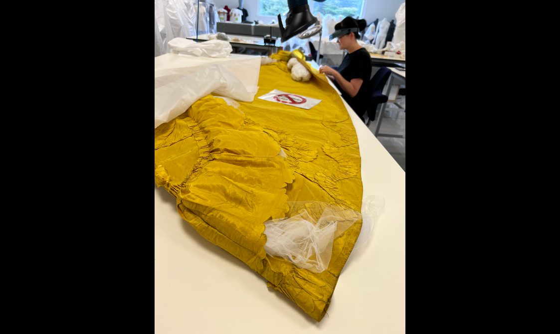 A yellow garment showing signs of damage is being conserved
