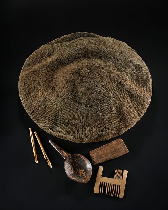 Brown knitted bonnet and small wooden personal belongings against a black background.