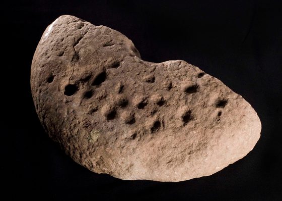 A tan piece of stone in a half circle shape with half circle indentation in the centre and a dimpled surface.