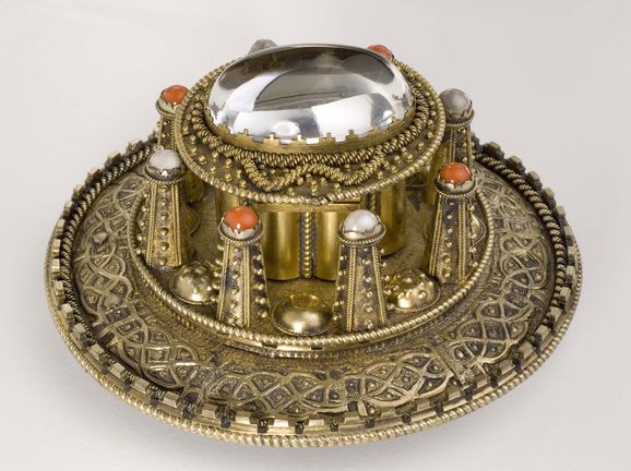A side view of a round gold coloured metal brooch with raised decoration.