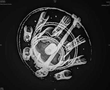 A black and white x ray of a raised round brooch.