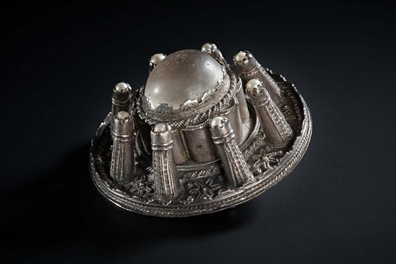 A side view of a round silver metal brooch with raised decoration.
