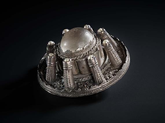 A side view of a round silver metal brooch with raised decoration.
