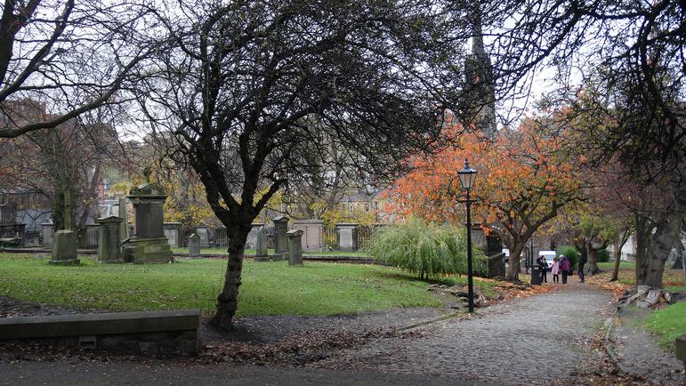 A photograph of a church grave yard with a path, trees and a lamp.