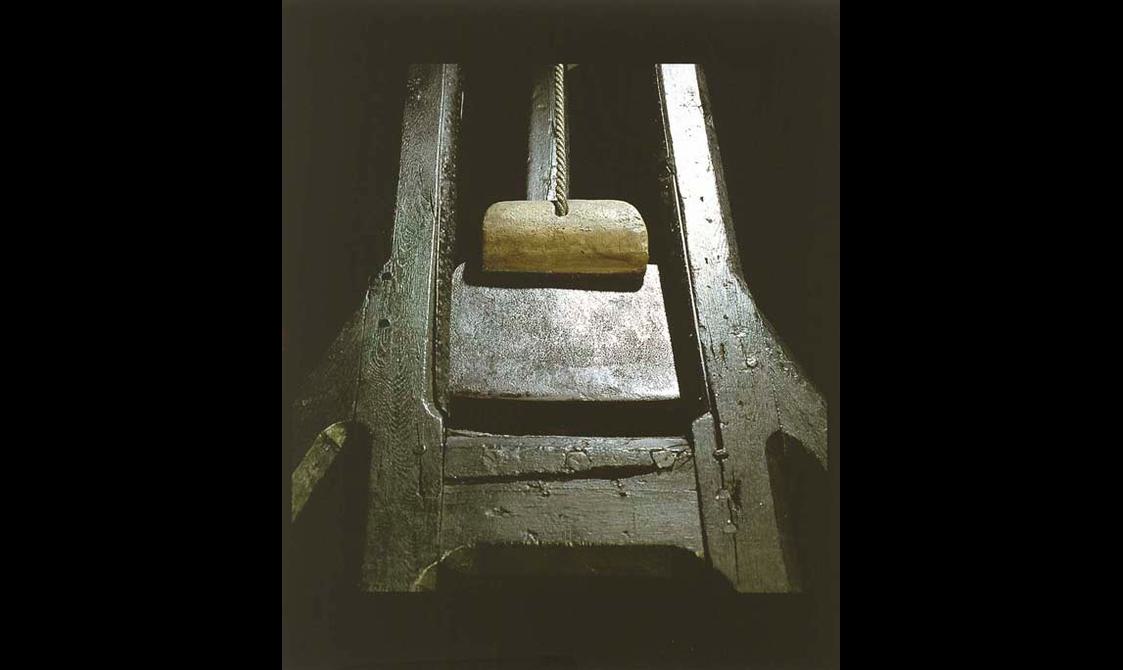 A blade suspended from the top of a wooden guillotine.