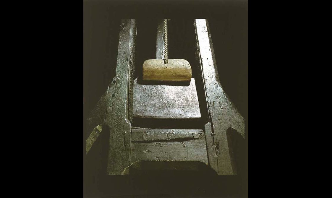 A blade suspended from the top of a wooden guillotine.