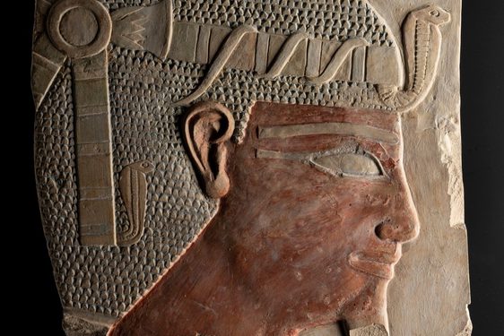 A stone carving of an Egyptian figure's head wearing a headdress viewed from the side.
