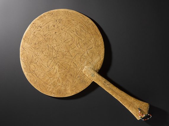 A wooden looking, round topped flat panel, with a loop fitted through the hand. There appears to be etched decoration on the panel back.