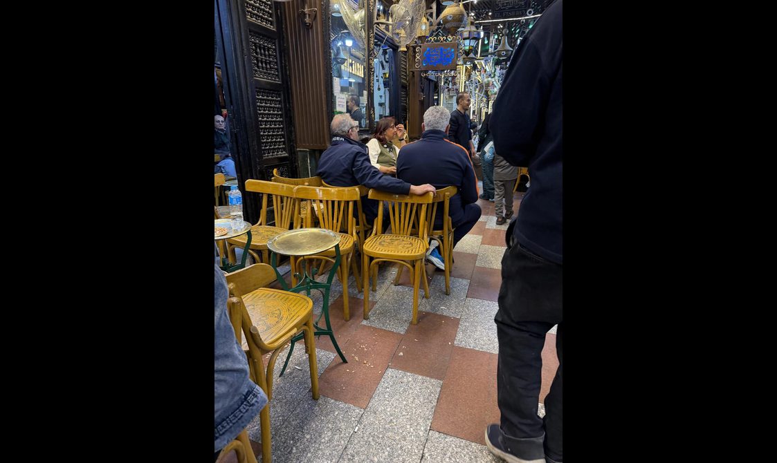 People sitting on ahwa chairs outside a café.
