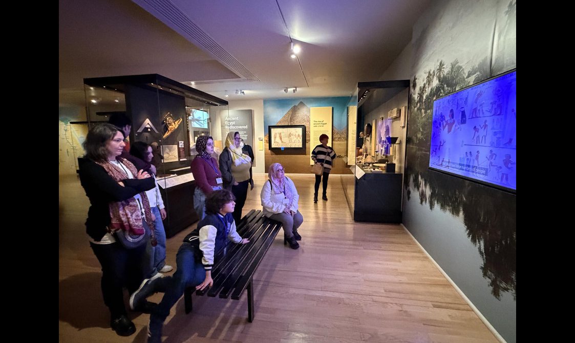 A group of people sit in a museum gallery watching a video about Egypt.