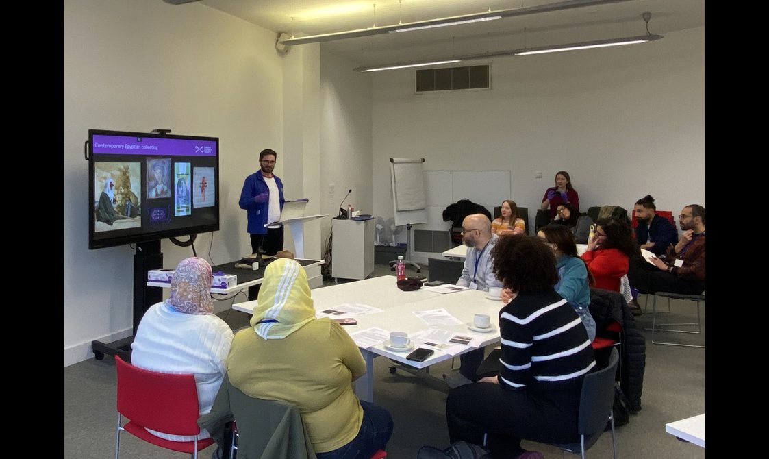 A museum curator, Dan Potter, giving a talk to a room of people. Dan is standing in front of a screen with images of objects from the National Colleciton.