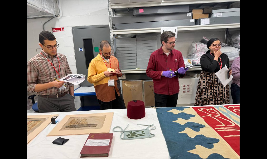 Four people stand examining different colourful Egyptian textiles in a museum store.