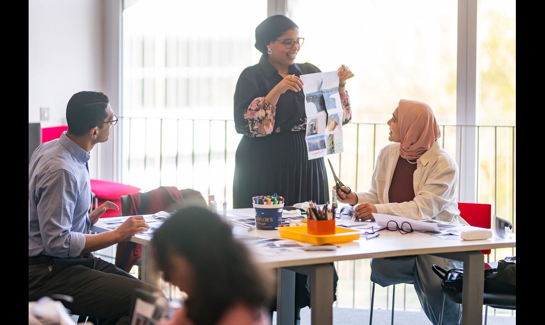 People show zine designs to each other while sitting at a table.