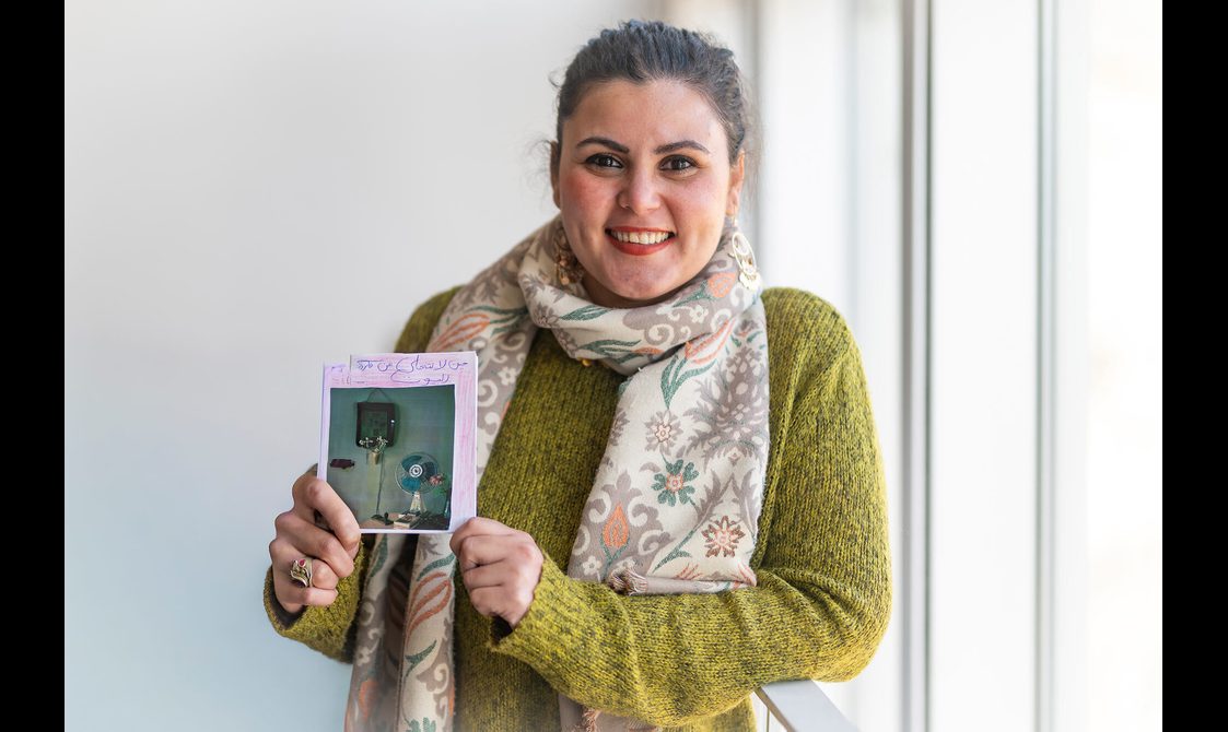 A woman wearing a green jumper and patterned scarf holding a zine she designed.