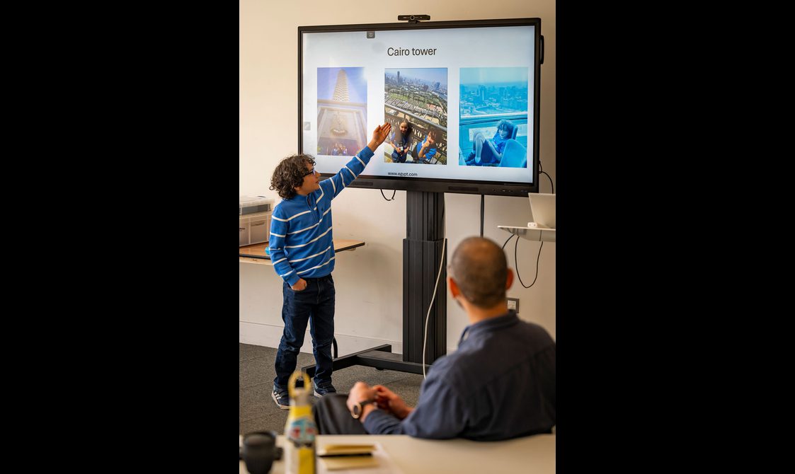 A child gives a talk to a group of people. They are pointing at pictures on a screen. The pictures show different locations in Egypt.