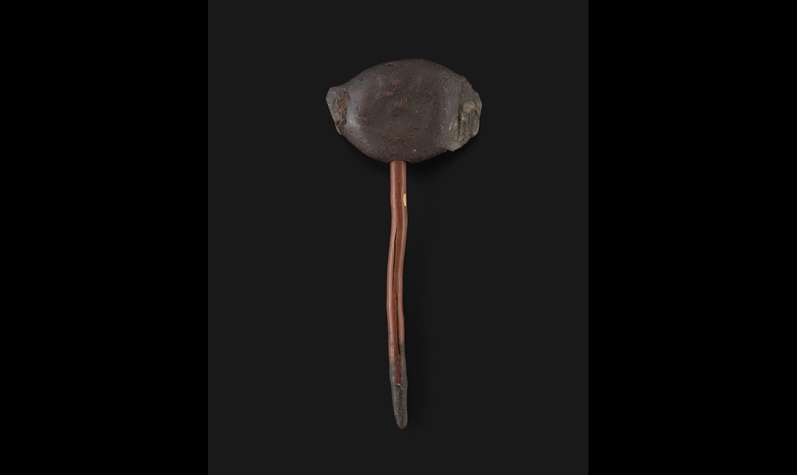 A small axe made from a slim piece of wood with a circular piece of resin at the top with two pieces of basalt on each side