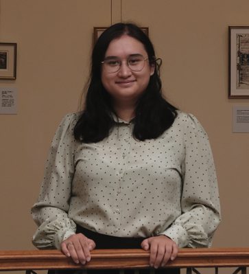 A woman dressed in a white polka dot blouse holding on a balustrade.