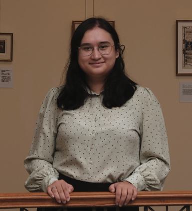 A woman dressed in a white polka dot blouse holding on a balustrade.