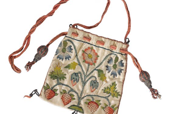 Square shaped purse decorated with blue and red flowers at the top, and six strawberries at the bottom. A red string attached to the top of thee purse, and three black tassels hang at the bottom of the purse.