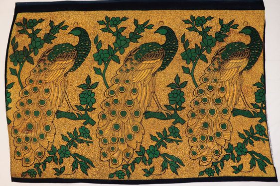 Gold textile with pattern of large black and green peacocks perched on branches.