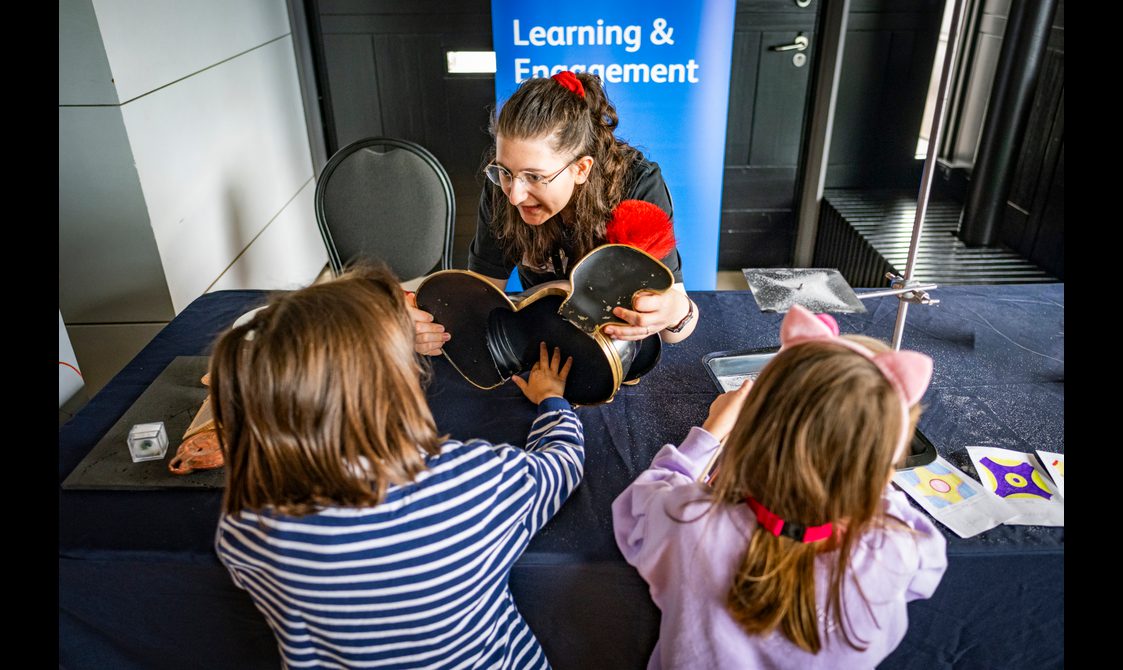 Two girls explore handling objects on a table during a museum session.