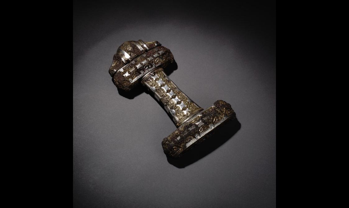 A sword hilt assembled from three rectangle parts in a shape of a horizontal letter H with a rounded triangle-shaped part at one end. Inlaid with non-descriptive silver organic shapes throughout.