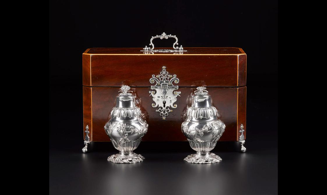 Wooden rectangular box with ornate silver handle on the lid, legs and ornate lock mechanism with fleur de lis motifs. Two silver containers with floral motifs throughout.