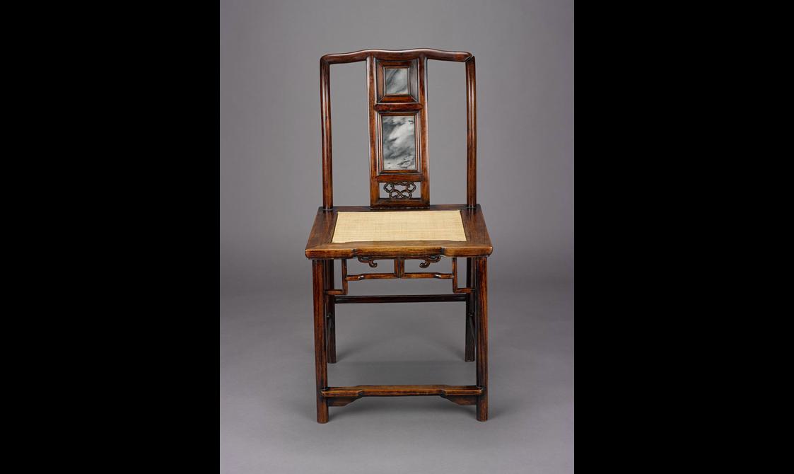 A decorative dark brown-red wood chair with a light yellow fabric in the middle of the seat