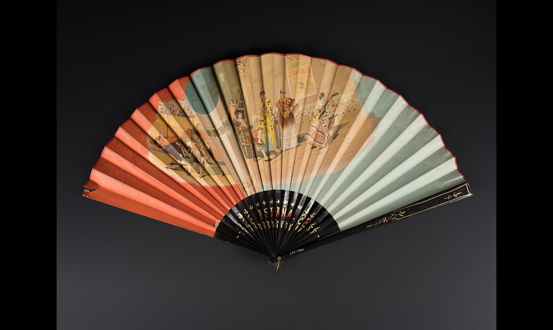 Decorative fan with wood sticks and guards painted black with gilt red and green painted details. paper leaf printed with a coloured design featuring a bullfighter and three women, one playing guitar.