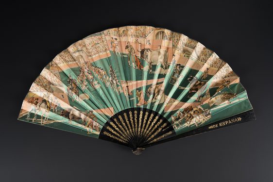 Fan with wooden sticks and guards painted black with gilt detailing. One guard with inscription 'ESPANA'. Fan leaf in metallic paper printed with a bullfighting scene