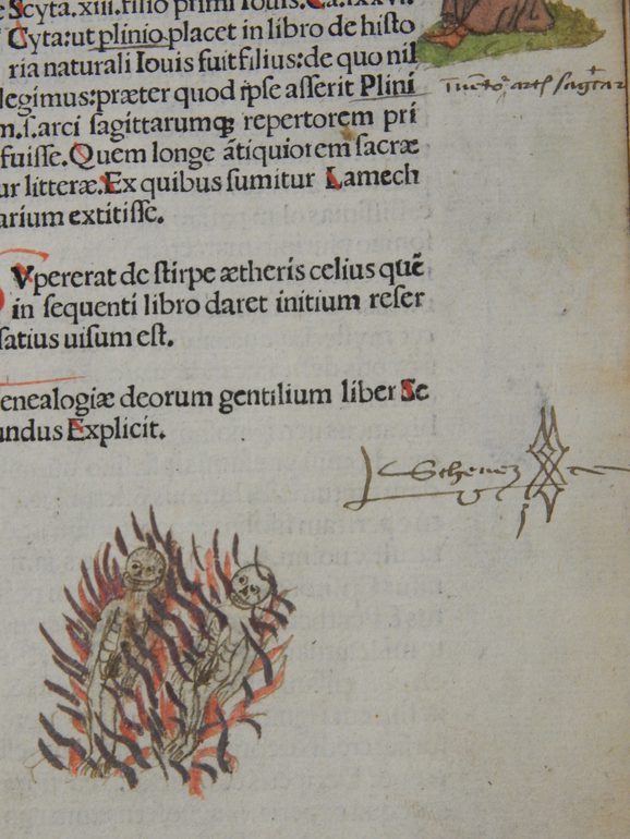 A written signature on a page of a book, which sits to the right of an illustration of two figures which appear to be on fire.
