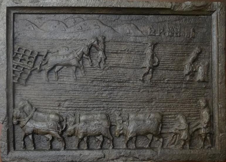 A replica of a tomb stone. The top half depicts a man and woman sowing the seed, as a horse-drawn harrower quickly covers the seeds with soil behind them.