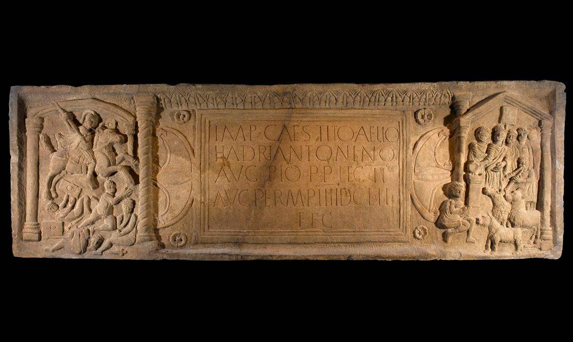 Large, rectangular slab with a central inscription flanked by deeply-carved engravings of cavalry, civilians with livestock and columns.