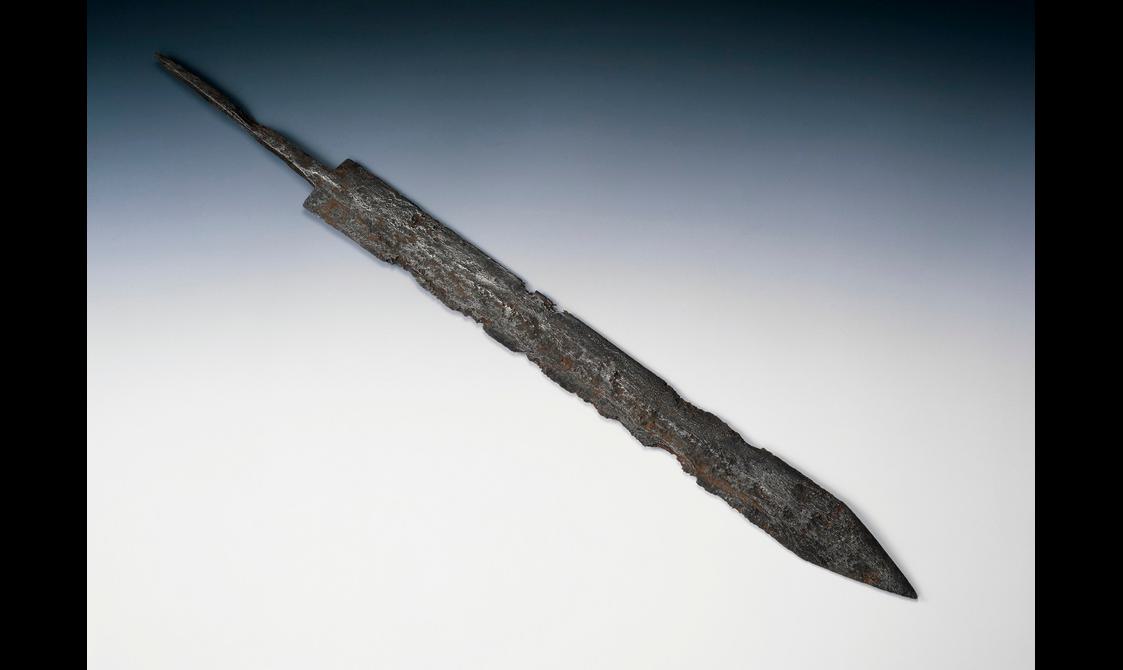 A classic Roman gladius with triangular point, straight blade and narrow tang set against a grey-blue background.