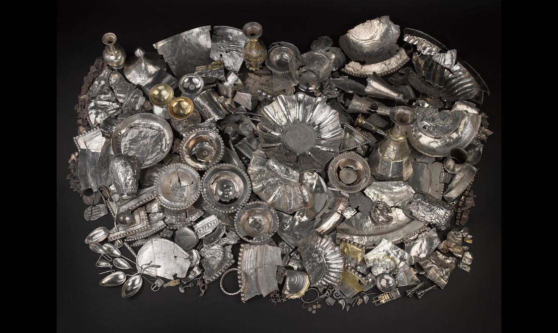 A huge pile of silver objects on a black background, from plates and vessels to tiny fragments and a large bowl in the centre.