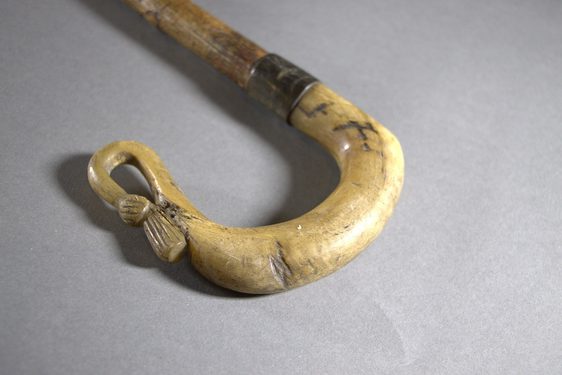The curved end of a shepherd's crook, showing a thistle emblem at the very end.