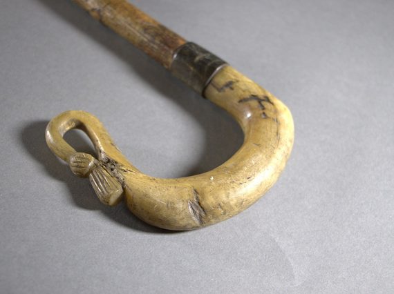The curved end of a shepherd's crook, showing a thistle emblem at the very end.