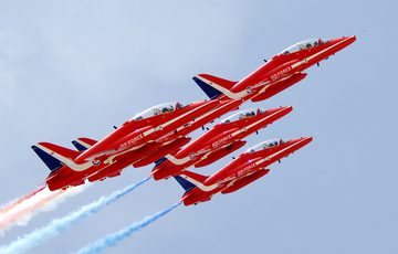 Five red planes fly in formation with red and blue smoke streams coming out of their engines.