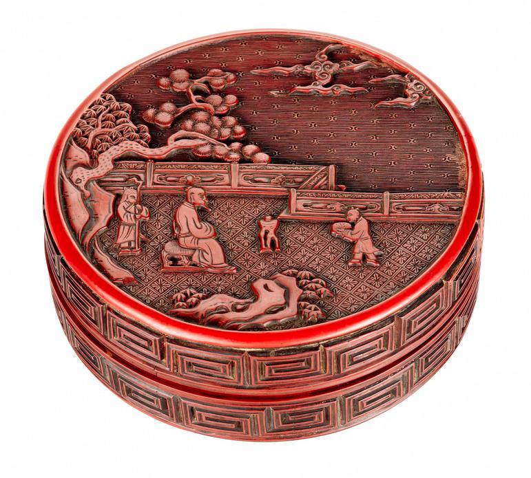 A small circular red box decorated with a sage seated in a garden flanked by two attendants, with thunder pattern on side.