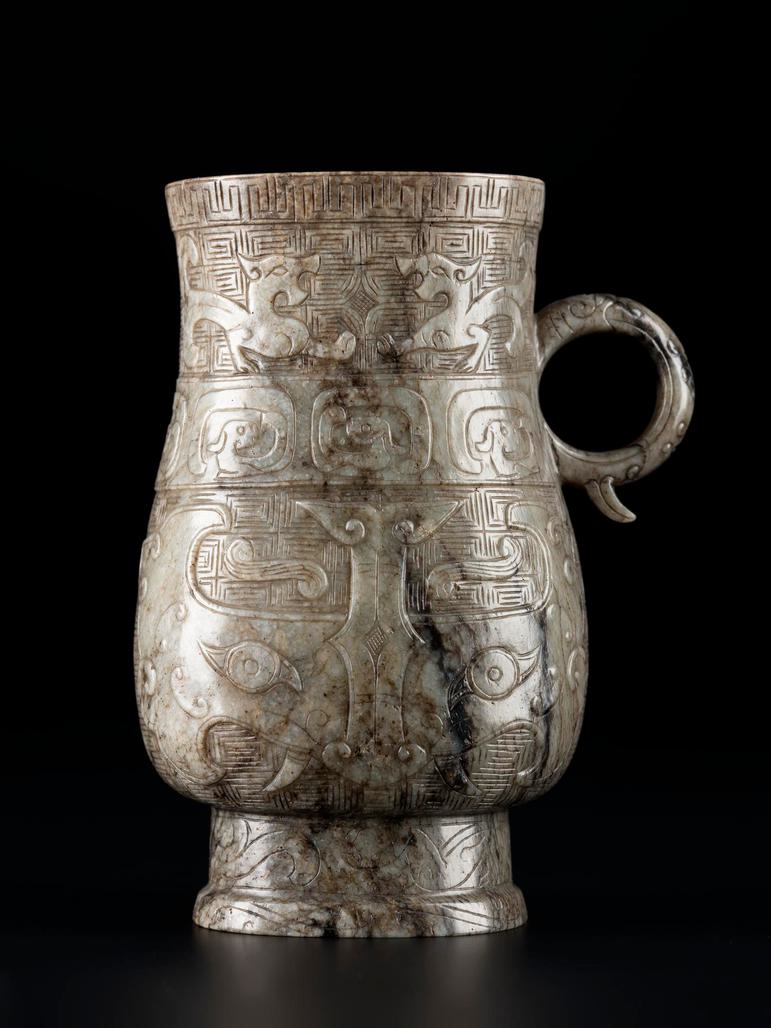 A worn jade green vase with a highly decorated surface and a small loop handle on its right