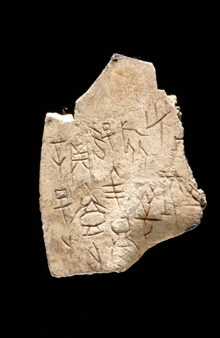 A sandy coloured piece of rock with inscriptions on the surface