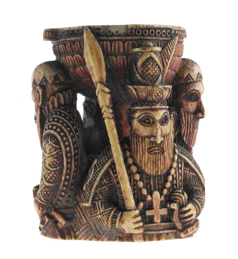 A sculpture of three figures in decorative clothing and jewellery with beards. The figures are placed round the base of a decorated semi-circle.