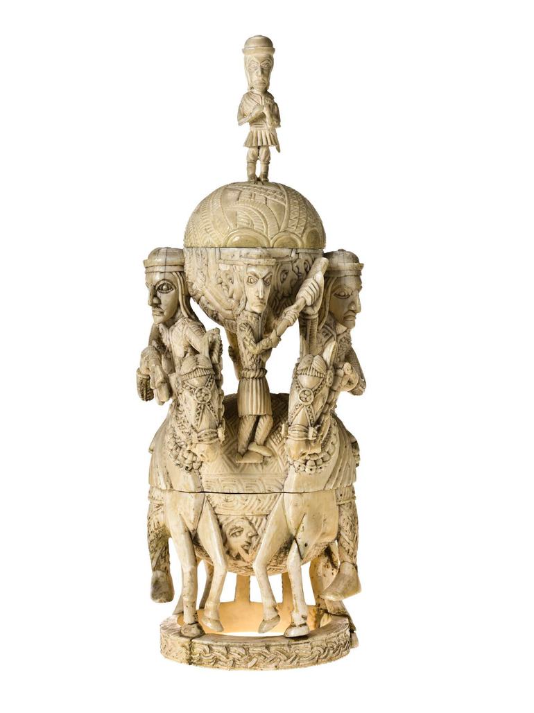 Tall off-yellow ivory sculpture. Two figures on horseback flack two orbs, on atop the other. A small human figure stand between the orbs, another crowns the sculpture.