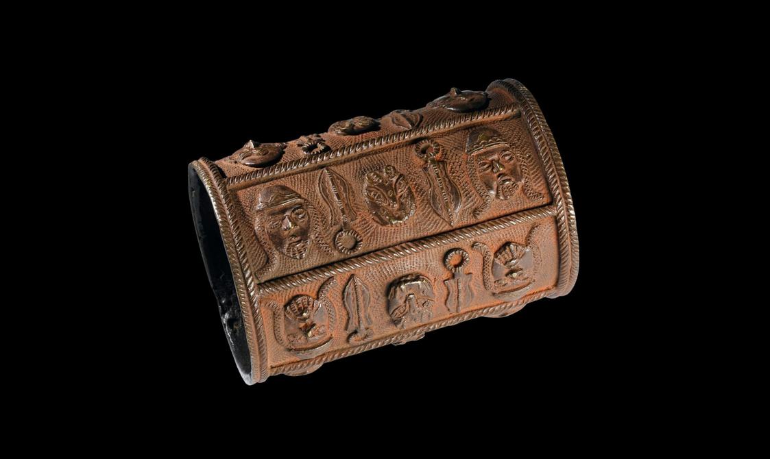 A brown cuff with carved faces and objects.