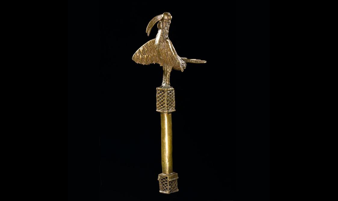 A brass pole with a latticed square at each end and a decorative bird on top.