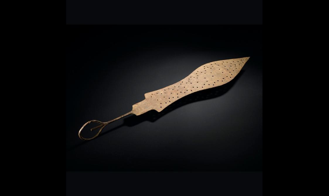 A spear shaped brass object with small holes punched on its surface. It has a thin handle with a loop at the end.
